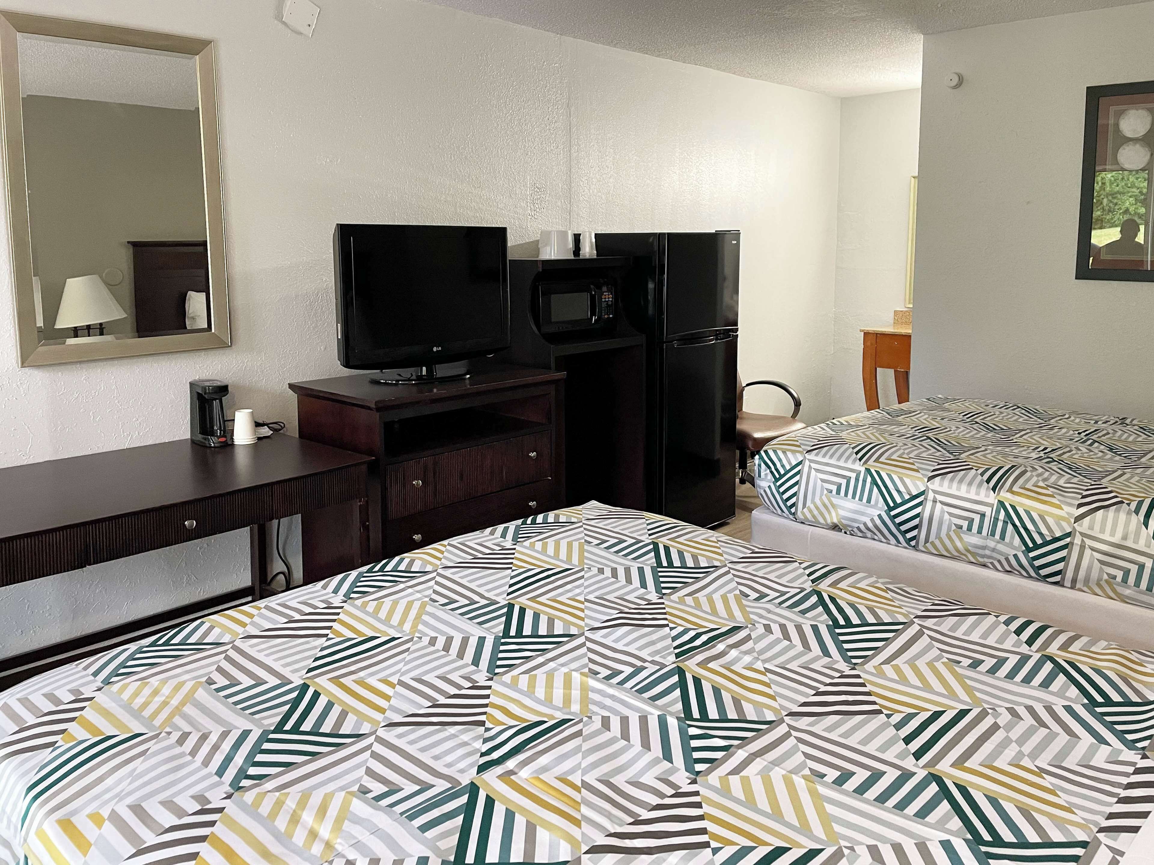 A hotel room with two beds, a TV, a refrigerator, a coffee maker, and a mirror.