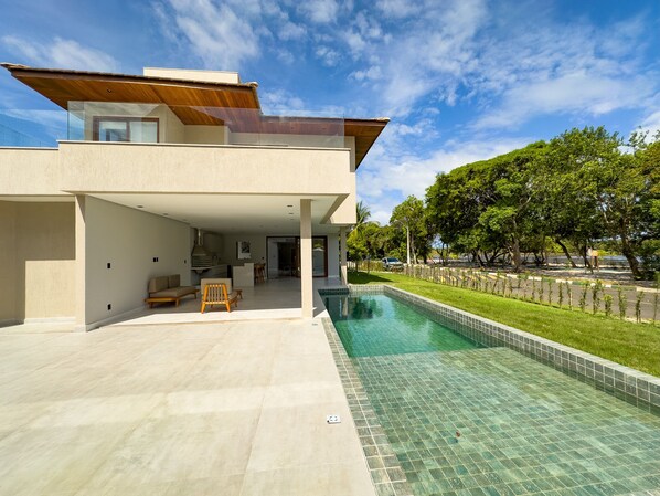 A modern house with a swimming pool, a covered patio, and a view of a tree-lined street.