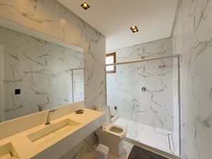 A modern bathroom with a marble backsplash, a large mirror, a sink, a toilet, and a glass shower enclosure.