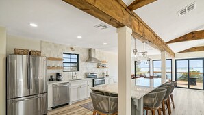 A modern kitchen with stainless steel appliances, a central island with bar stools, and a large window overlooking the ocean.