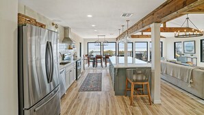 A modern kitchen with a stainless steel refrigerator, wooden beams, and large windows offering a view.