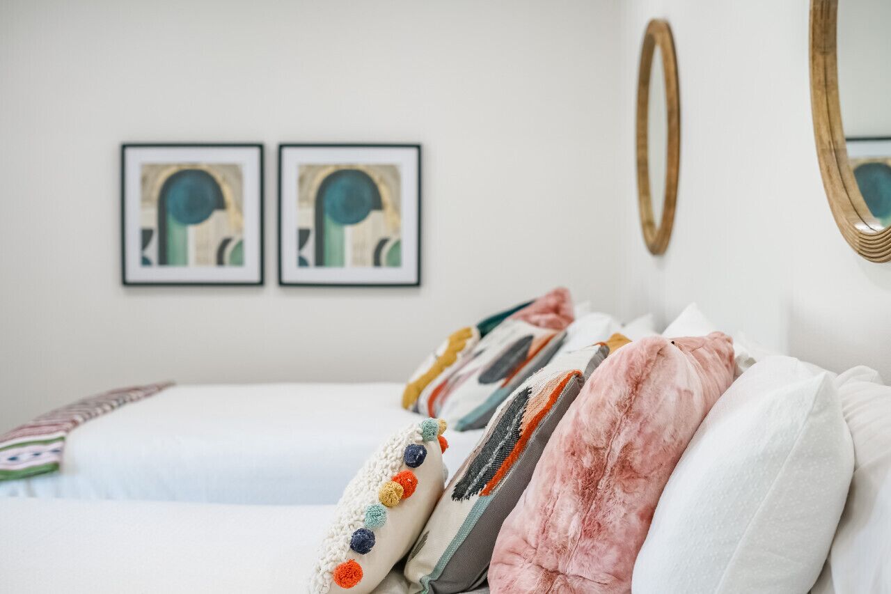 Una cama bien hecha con almohadas coloridas y un espejo grande en la pared.