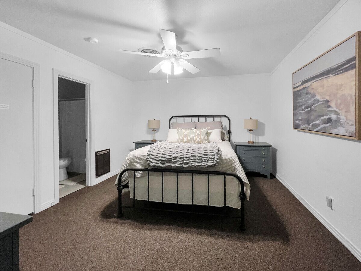 A bedroom with a bed, a ceiling fan, a nightstand, a dresser, and a painting on the wall.