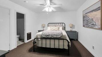 A bedroom with a bed, a ceiling fan, a nightstand, a dresser, and a painting on the wall.