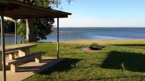 Un espace pique-nique équipé d’un banc et d’une table de pique-nique couverte, avec vue sur un lac.