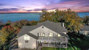 Une maison à deux étages avec un balcon, entourée d’arbres et offrant une vue sur une vaste étendue d’eau.