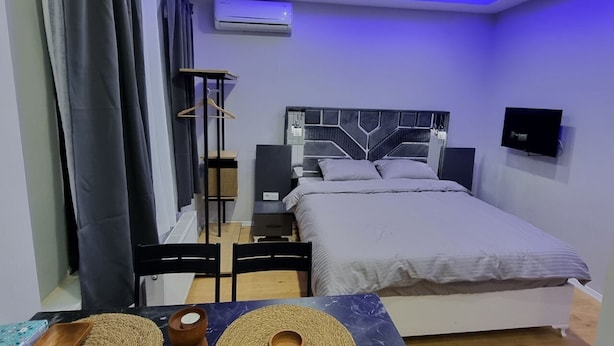 A modern bedroom with a bed, bedside tables, a TV, and a table with decorative mats. - Amur 205 (Istanbul)