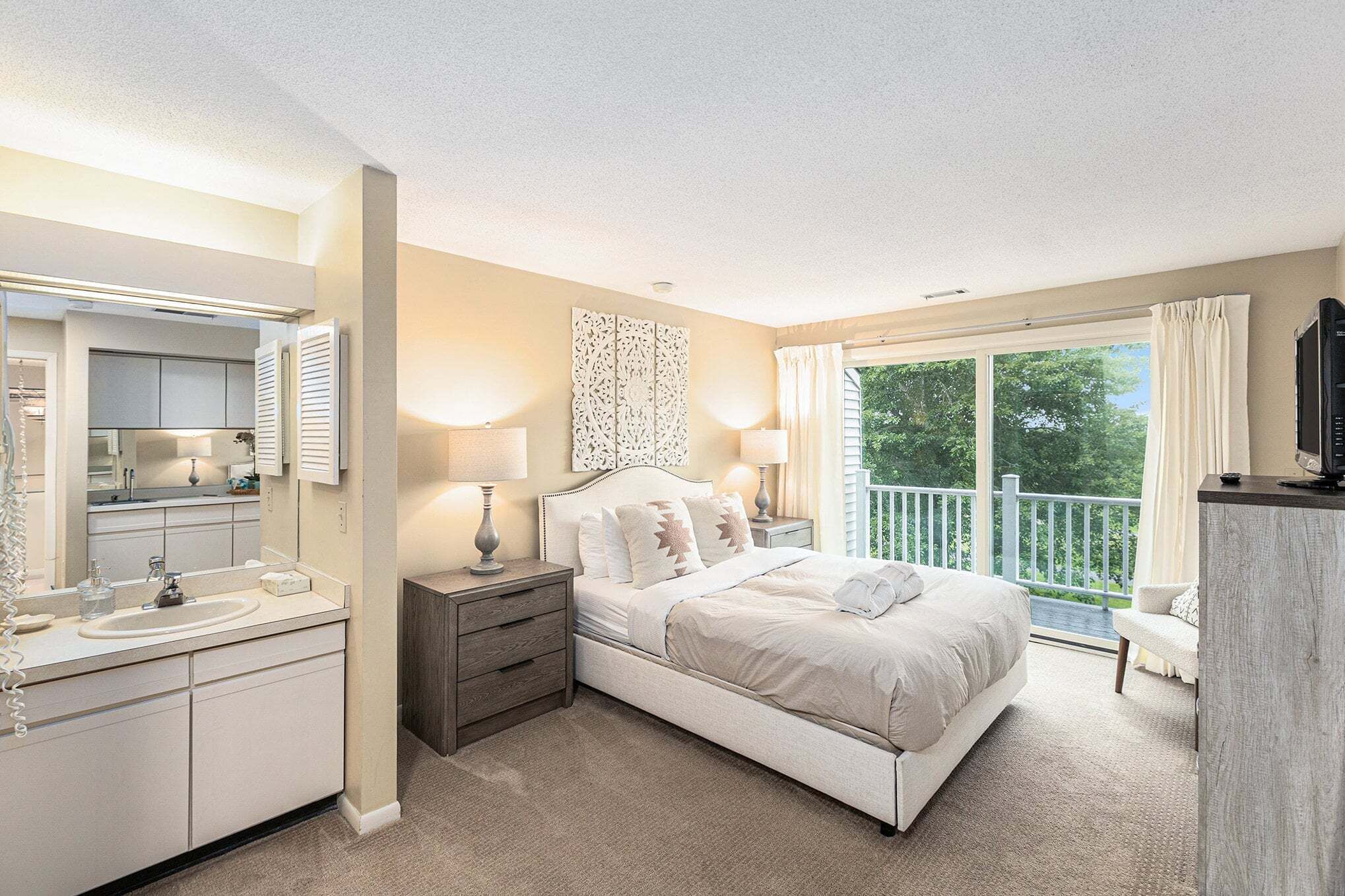 Quarto com cama, mesas de cabeceira, espelho, cômoda e varanda com vista.