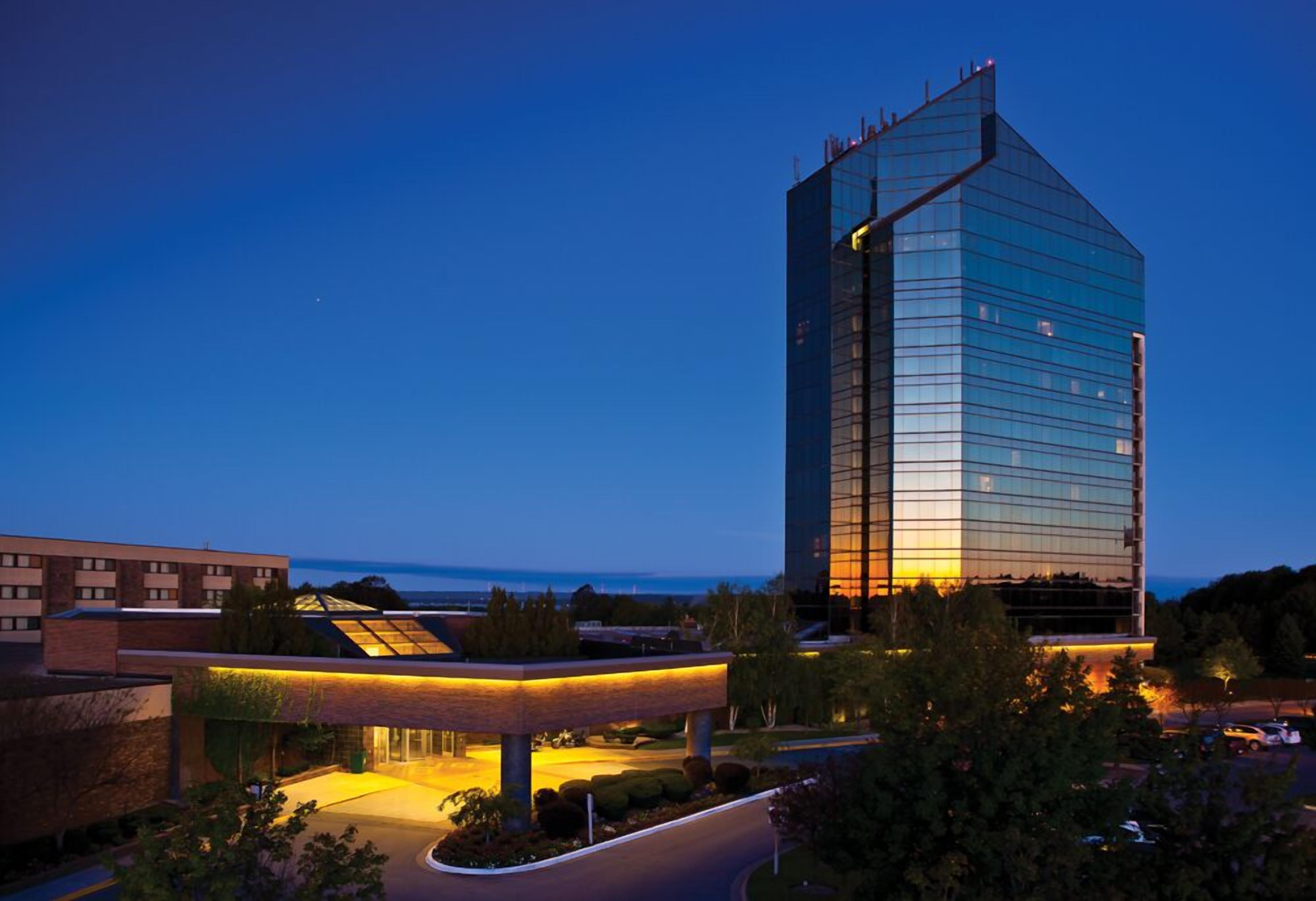A modern hotel with a prominent glass facade, a covered outdoor area, and a view of the ocean.