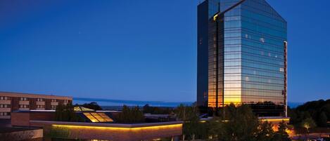 A modern hotel with a prominent glass facade, a covered outdoor area, and a view of the ocean.