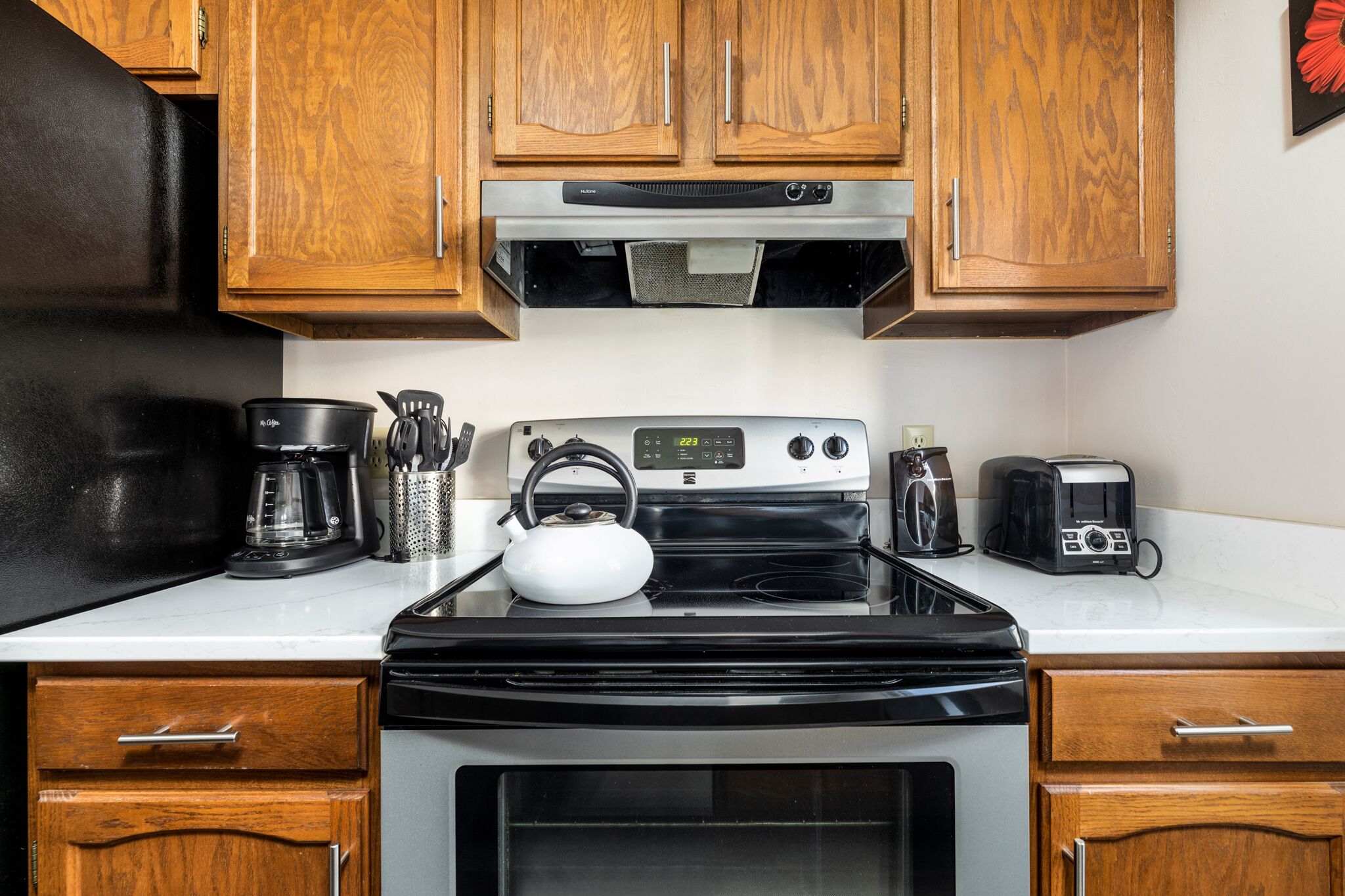 A kitchen with wooden cabinets, a black stove, a coffee maker, a kettle, and a toaster.
