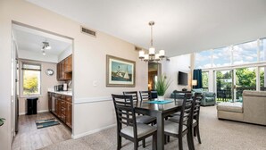 A dining area with a table, chairs, a chandelier, a painting, and a view through large windows. - 2BDR Loft Suite Golf Course Condo 5549 (Williamsburg)