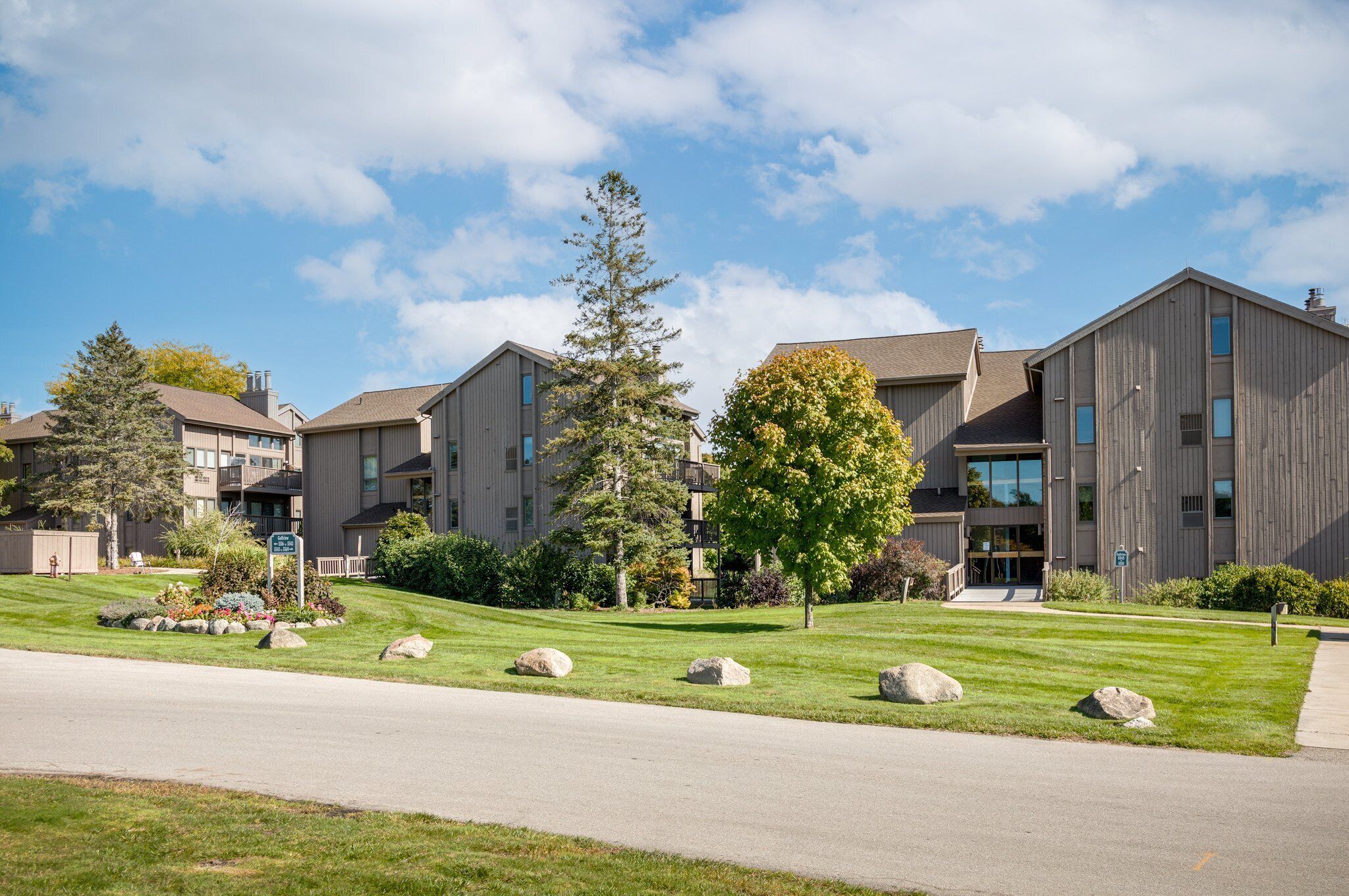 A modern apartment complex with multiple buildings, well-maintained lawns, and a clear sky.