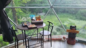 Una habitación acogedora con una mesa lista para dos personas, una cesta de mimbre con aperitivos, un libro y una figurita de un oso sosteniendo un cartel.
