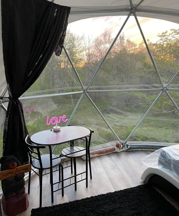 A room with a large glass dome window, a small round table with chairs, a bed, and a teddy bear.