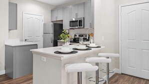 A modern kitchen with grey cabinets, a central island with bar stools, a microwave, and a refrigerator. - Stylish 2BR Scottsdale, Pet-friendly, Sunrise Peak (Scottsdale)