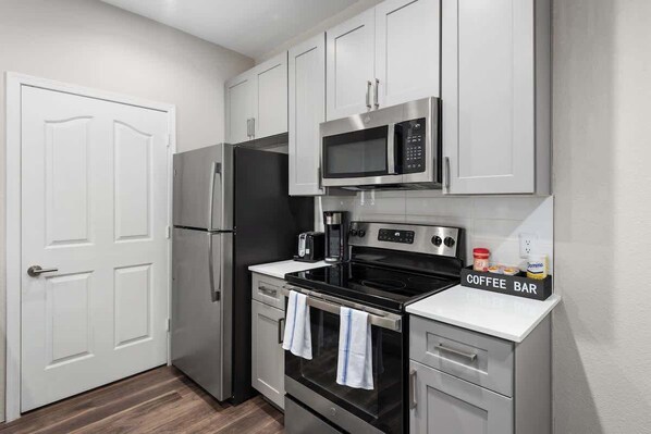 A compact kitchen with a refrigerator, microwave, stove, and a coffee bar setup.