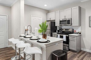 A modern kitchen with white cabinetry, stainless steel appliances, and a central island with bar stools.
