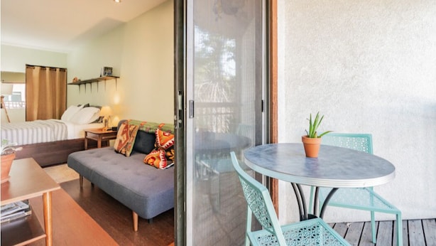 Una habitación con una cama, un sofá, una mesa con sillas y un ventanal corredero que da a un espacio exterior con mesa y sillas.