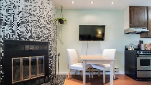 Una cocina moderna con un salpicadero de azulejos negros, un televisor de pantalla plana sobre una mesa de madera con sillas, un horno empotrado y una planta colgante.