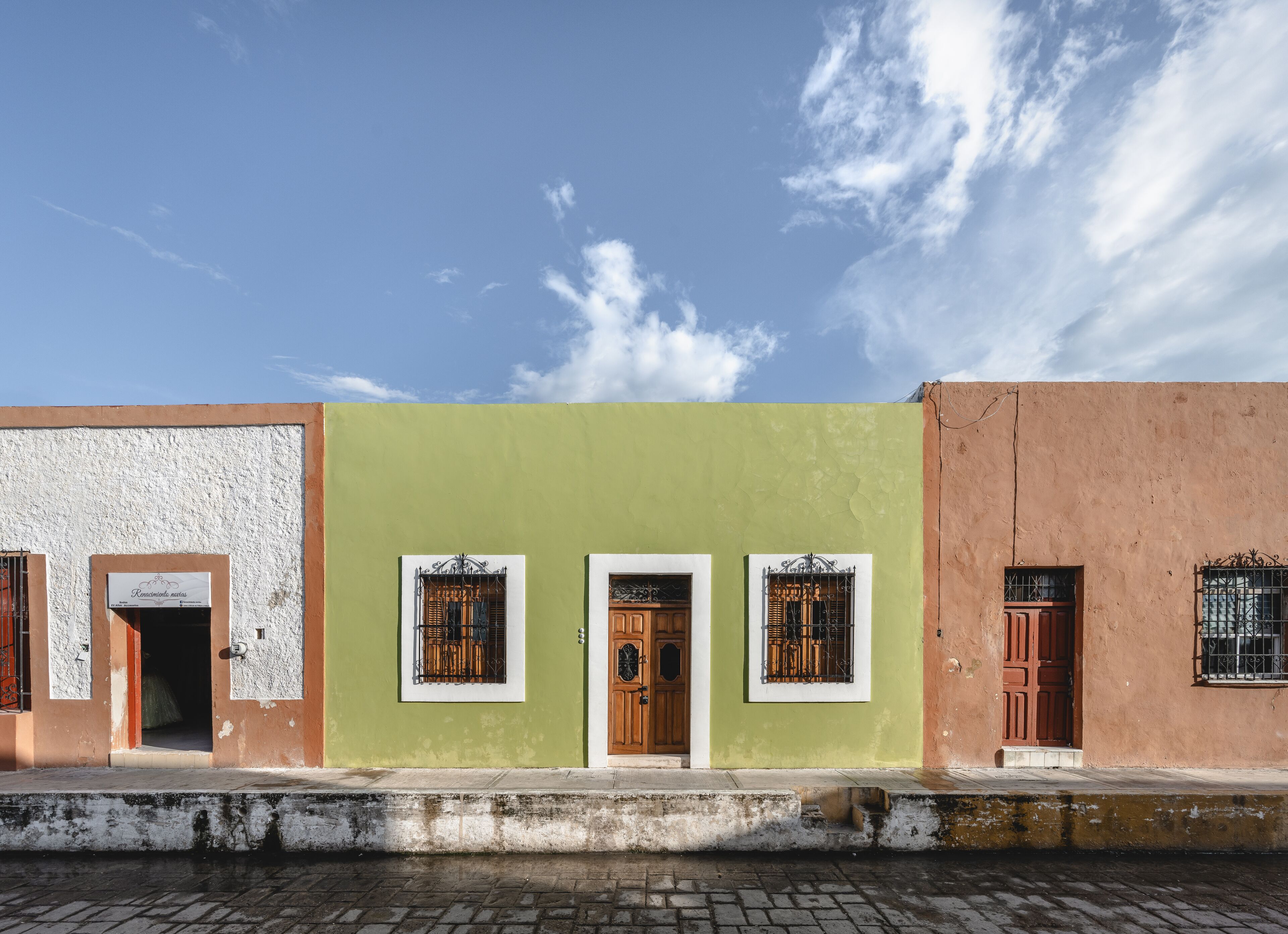 A row of three buildings with distinct facades, each featuring a door and window with metal bars.