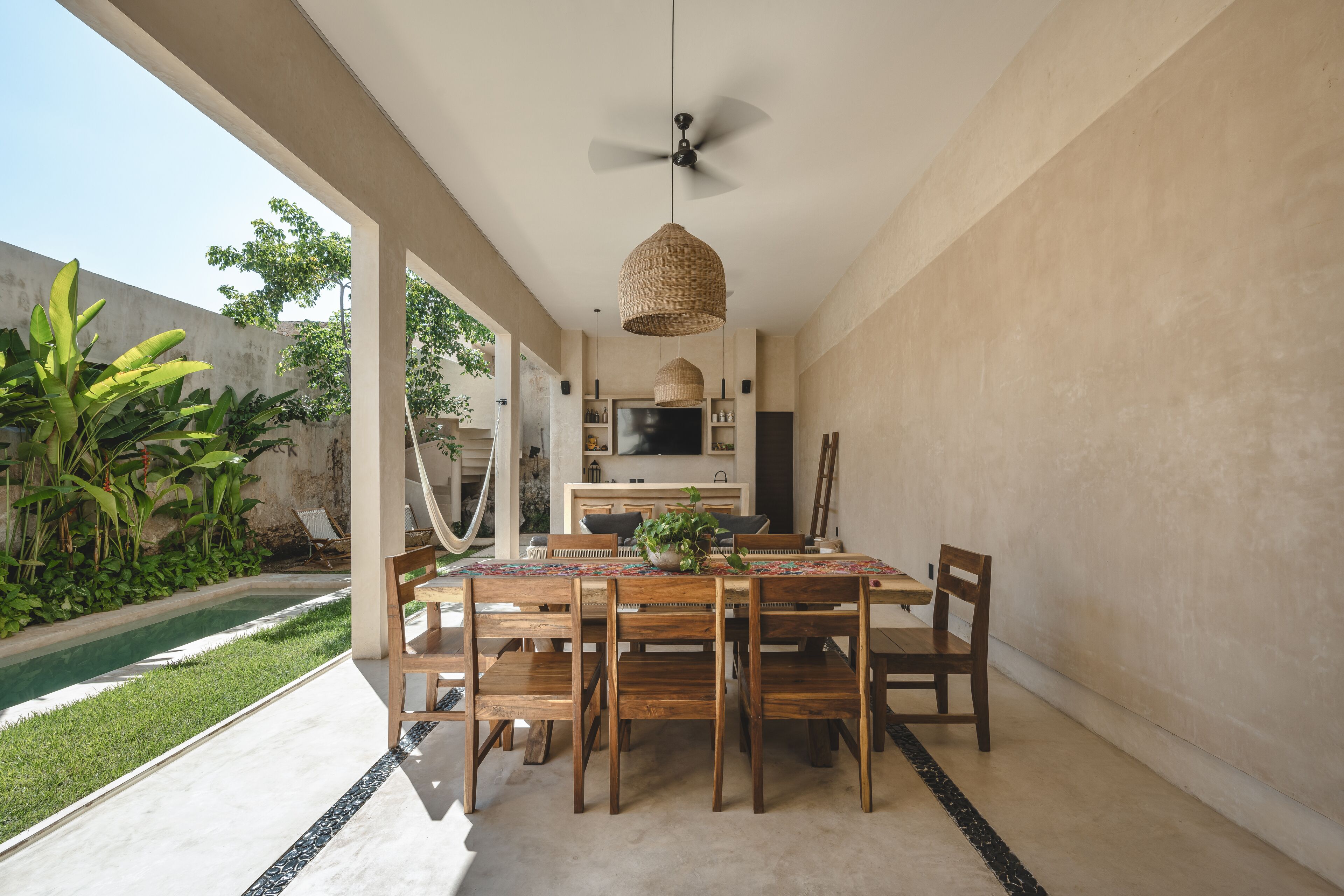 Un área de comedor al aire libre con piscina, sillas de madera y un ventilador de techo.