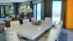 A modern dining area with a white table, white chairs, and a view of the ocean. - Villa Bonsai (Calheta)