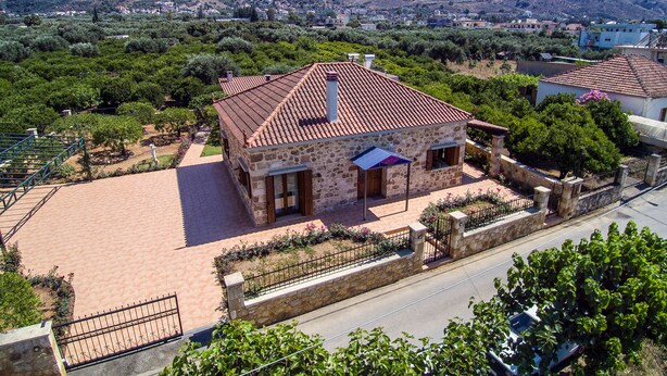 A stone house with a tiled roof, surrounded by a paved driveway and a stone wall.