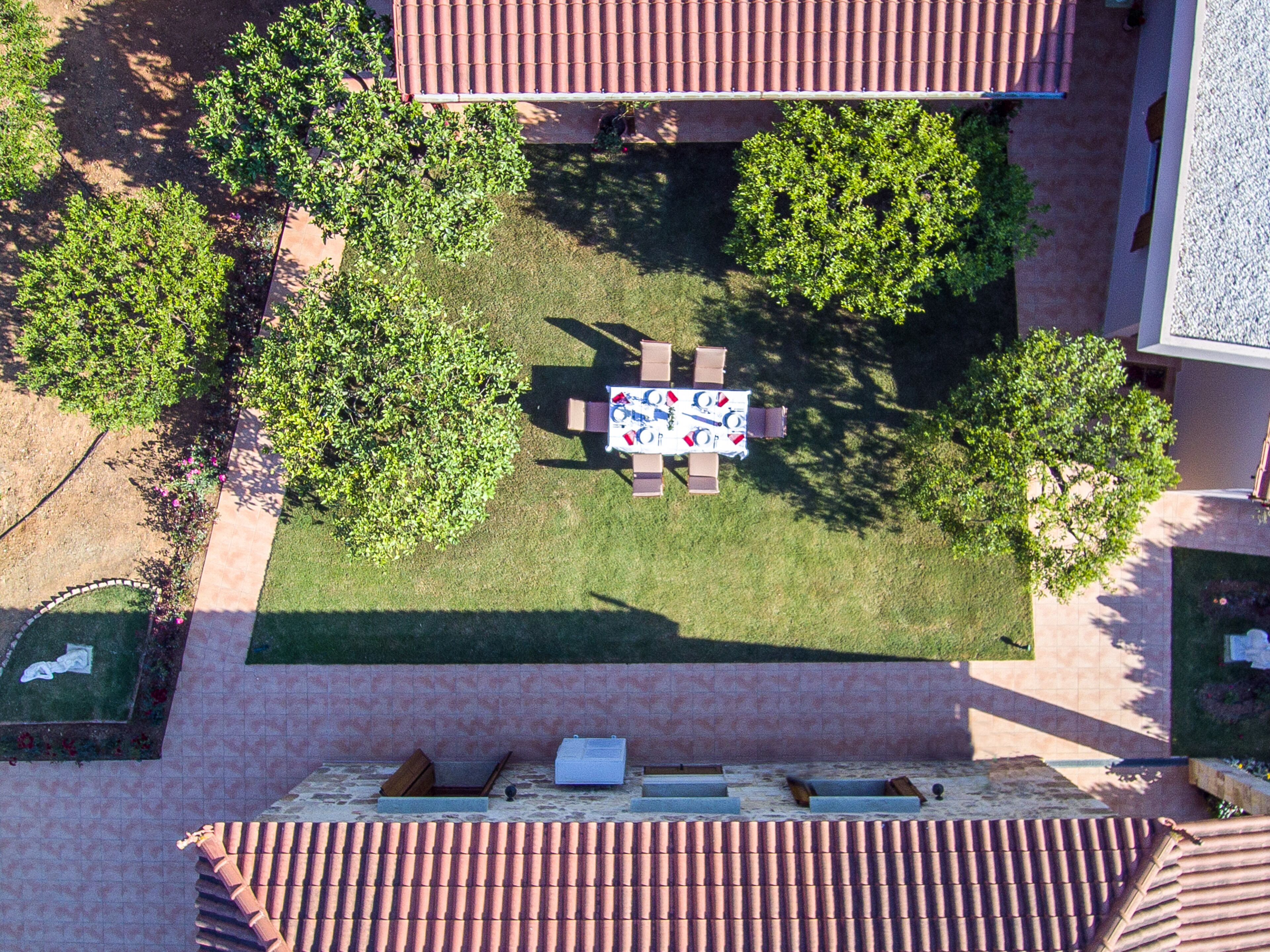 An aerial view of a courtyard with a tiled table and chairs, surrounded by trees and a building with a tiled roof.