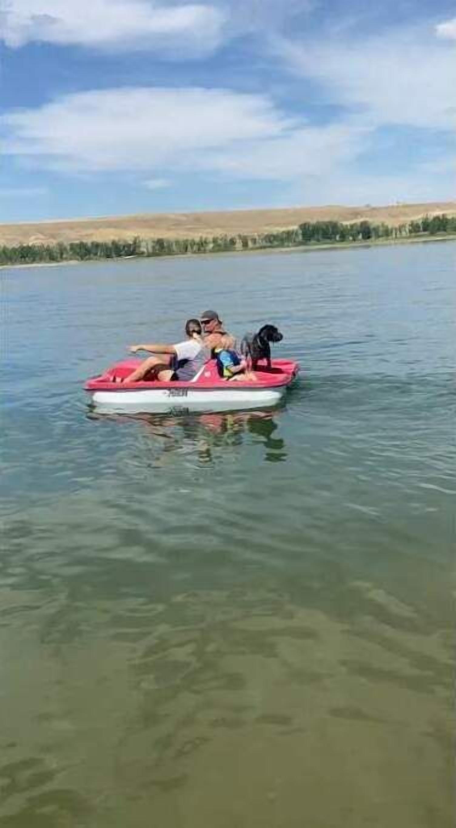 Una piccola imbarcazione gonfiabile rossa con tre persone e un cane su un lago calmo.