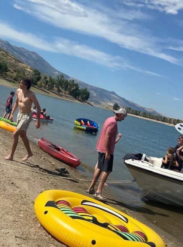 A lakeside scene with inflatable rafts and a boat. - Queen and twin bed Trailer on private beach, Hammocks, tiki torches, fishing (Clifton)
