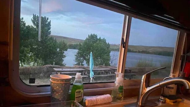 A kitchen area with a window view of a lake and trees. - Queen and twin bed Trailer on private beach, Hammocks, tiki torches, fishing (Clifton)