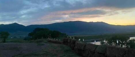 A rural landscape with mountains, a river, and a stone wall.