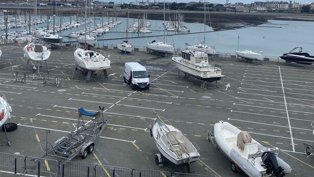 A marina with numerous boats docked, a van, and a few cars.