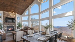 A spacious living area with a fireplace, comfortable seating, and a large dining table set for six. - Designer Home w/ Incredible Views, Sleeps 16 (Wintergreen Resort)