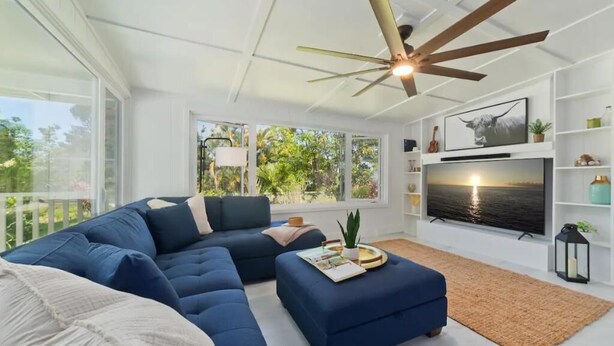 A modern living room with a sectional sofa, a coffee table, and a TV mounted on the wall. - Mountain Oasis: Modern Plantation Home (Kealakekua)