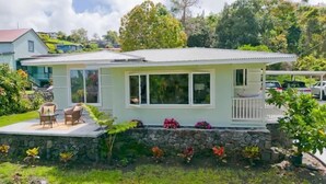 A single-story house with a porch, a small deck, and a stone wall foundation. - Mountain Oasis: Modern Plantation Home (Kealakekua)