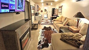 Ein Wohnzimmer mit Flachbildfernseher, der Streamingdienste anzeigt, einer Couch, einem Couchtisch und einem Kamin.