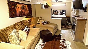 Ein Wohnzimmer mit einer Couch, einem Couchtisch, einem Fernseher und einer Küche im Hintergrund.
