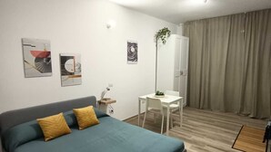 A modern hotel room with a large bed, a desk, and a chair. There are three paintings on the wall and a plant on the desk. - Appartamento Daisy - Parma (Parma)