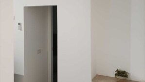 A hallway with a white wall, a wooden floor, a small plant on a shelf, and a door at the end. - Appartamento Daisy - Parma (Parma)
