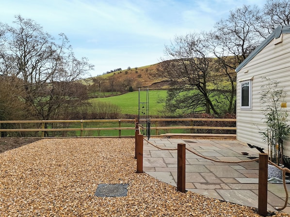 A gravel patio with a wooden fence, a metal gate, and a building with a window.