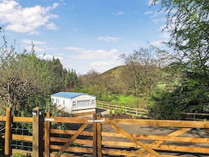 A white building with a blue roof, surrounded by greenery and a wooden fence.