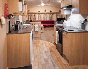 A compact kitchen with wooden cabinets, a stove, and a dining area with a red sofa.