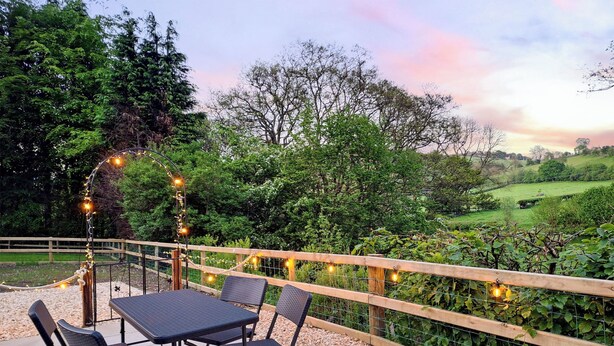 A patio with a table and chairs, surrounded by a wooden fence and string lights. - 2 bedroom accommodation in New Radnor, near Presteigne (New Radnor, near Presteigne)
