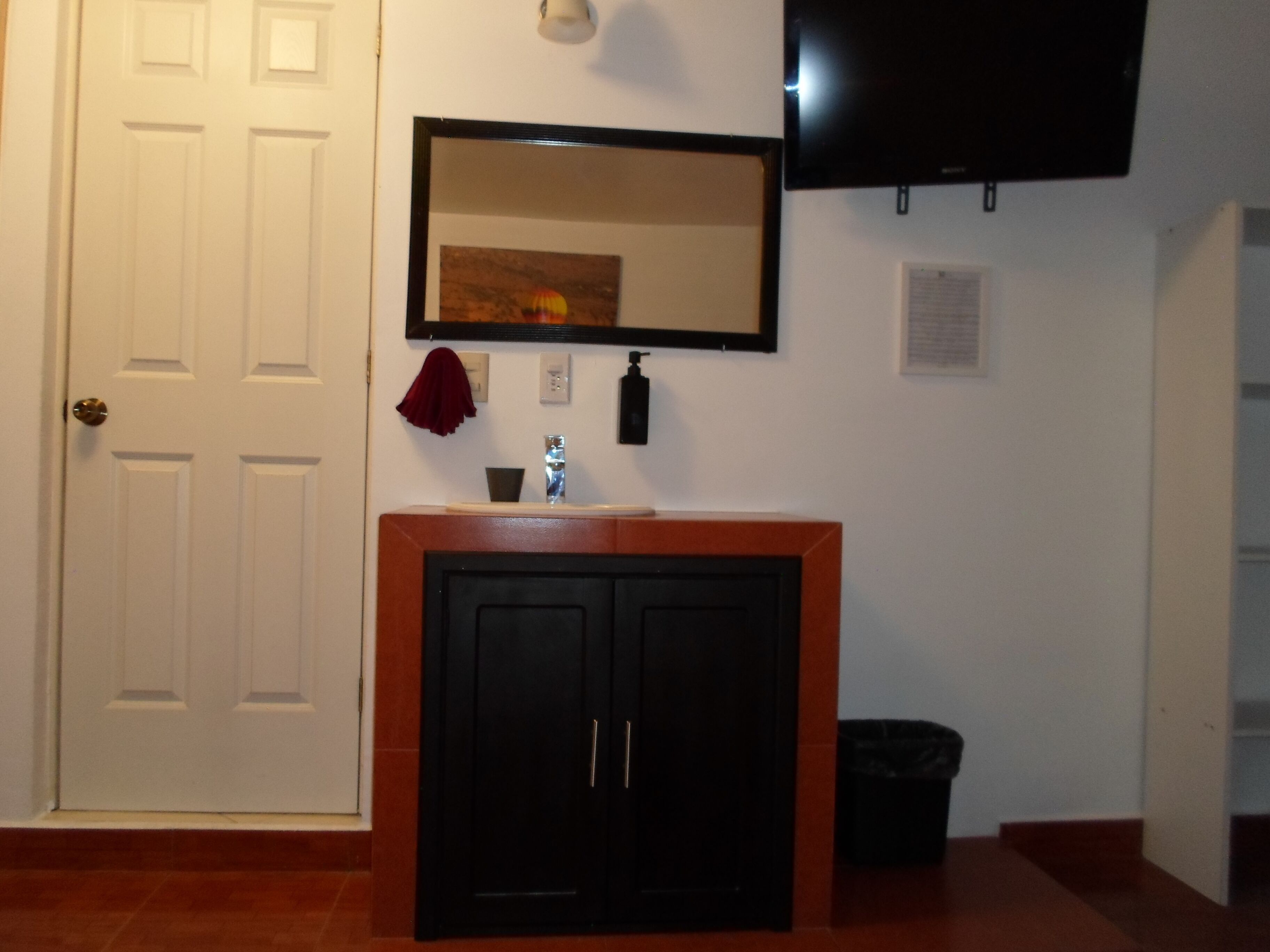 A room with a white door, a black cabinet, a mirror, and a television mounted on the wall.