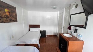 A hotel room with two single beds, a wooden headboard, a small bedside table, a bathroom with a sink, mirror, and a towel hanging on the wall. - Hotel María Bonita (Tlaxcala)