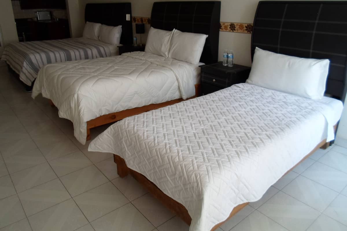 Habitación de hotel con tres camas, cada una con un diseño de cabecera diferente. Hay una pequeña mesa con una botella de agua.
