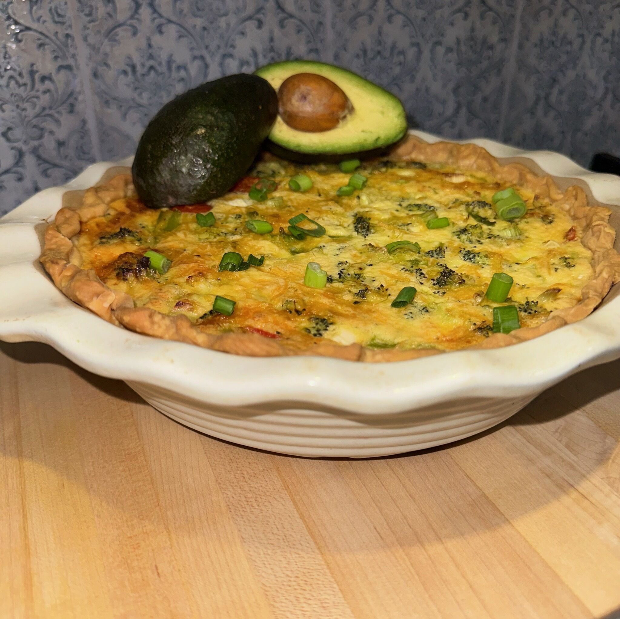 A quiche in a white ceramic dish on a wooden table.