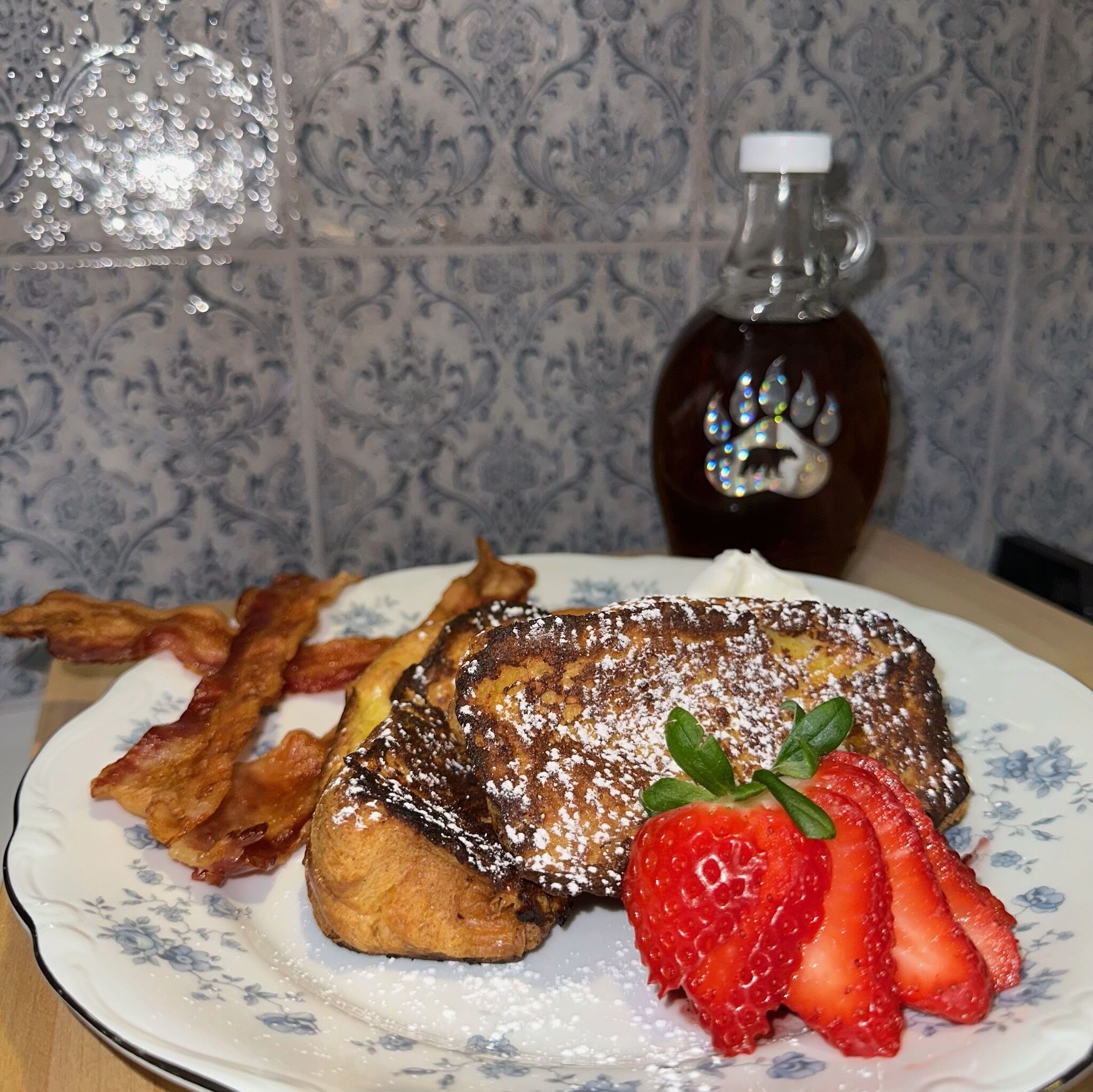 Un piatto con french toast, strisce di pancetta e fragole su un piatto a motivi floreali.